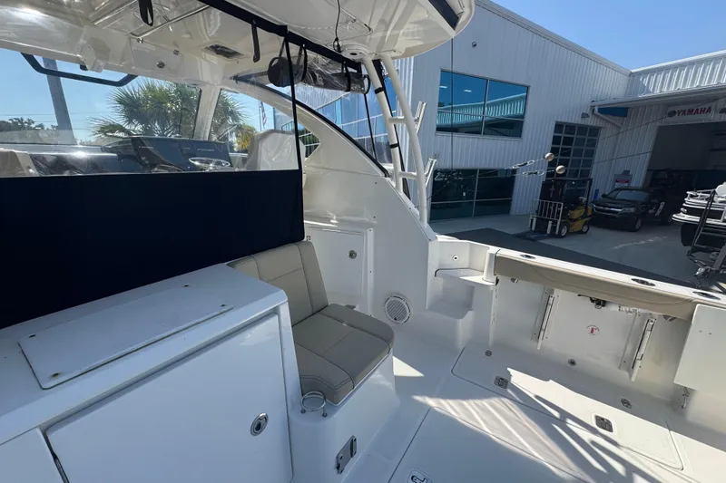 Slide: The Image of 2020 Pursuit OS 325 Offshore boat interior with seating and storage, docked near a modern building. - 4
