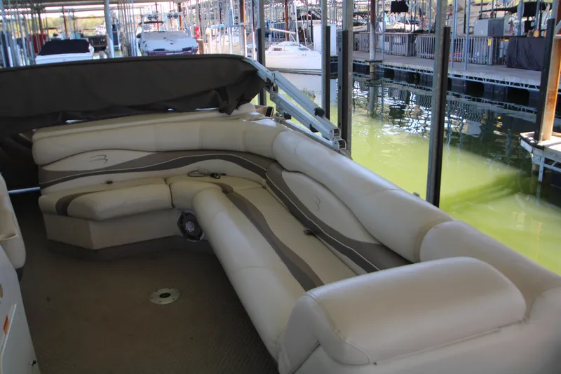 Slide: The Image of 2005 Bennington 2275FSi boat interior with white and beige seating, docked by green water. - 9
