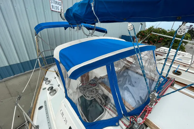 Slide: The Image of 1988 CAL 28 sailboat with blue canopy and visible rigging, docked near storage building. - 13