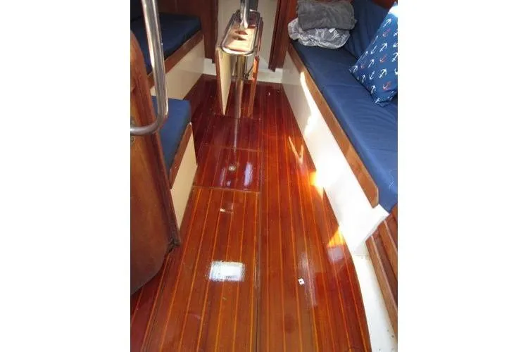 Slide: The Image of Interior of a 1988 CAL 28 sailboat with polished wooden flooring and blue cushioned seating. - 38