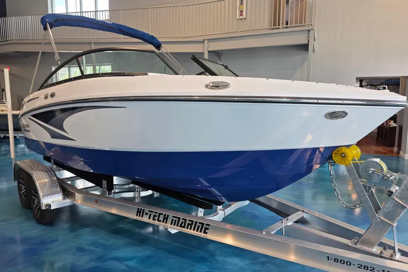 The Image of 2024 Monterey M-205 boat on trailer in showroom, featuring sleek blue and white design. - 0