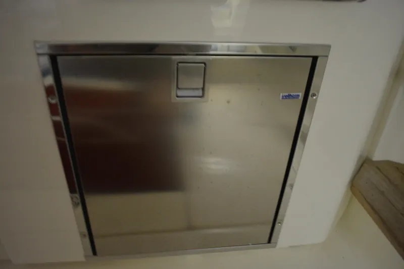 Slide: The Image of 2019 Boston Whaler 350 Realm interior storage compartment with yellow hose and wooden panel. - 24