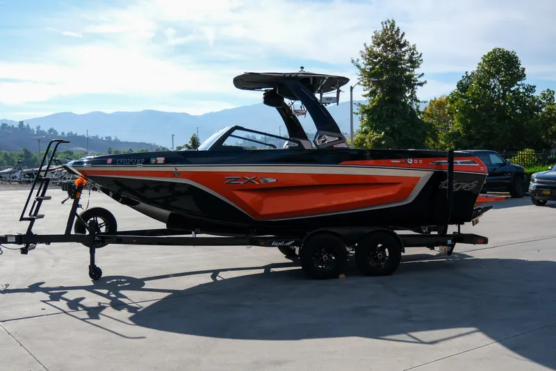 The Image of 2021 Tigé 21ZX boat on trailer, black and orange design, parked outdoors. - 1