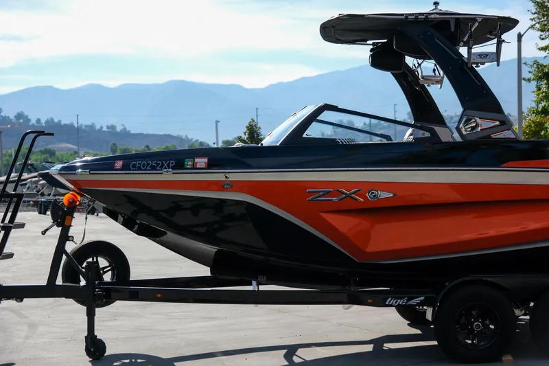 Slide: The Image of 2021 Tigé 21ZX boat on trailer, orange and black design, mountain backdrop. - 11