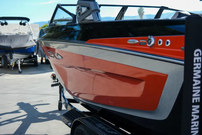 Slide: The Image of 2021 Tigé 21ZX boat in vibrant orange and black, displayed at a marina. - 29