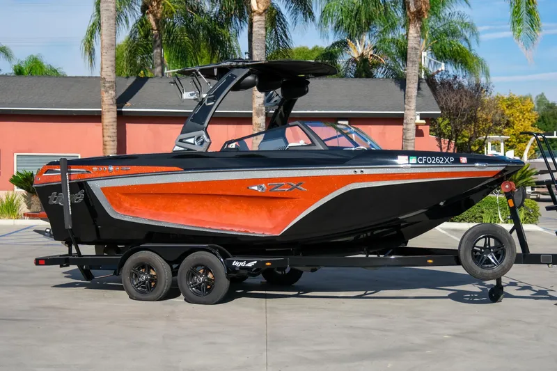 Slide: The Image of 2021 Tigé 21ZX boat in vibrant orange and black on a trailer, parked outdoors. - 5