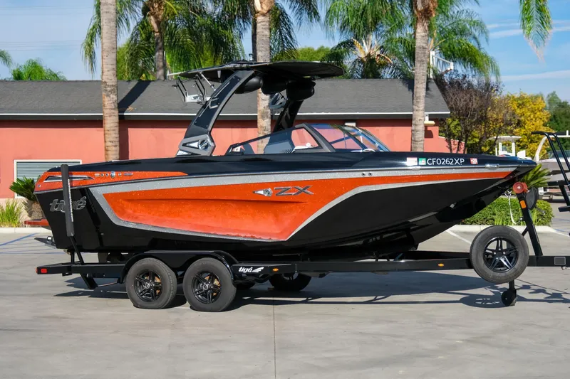 Slide: The Image of 2021 Tigé 21ZX boat on trailer, vibrant orange and black design, parked outdoors. - 6
