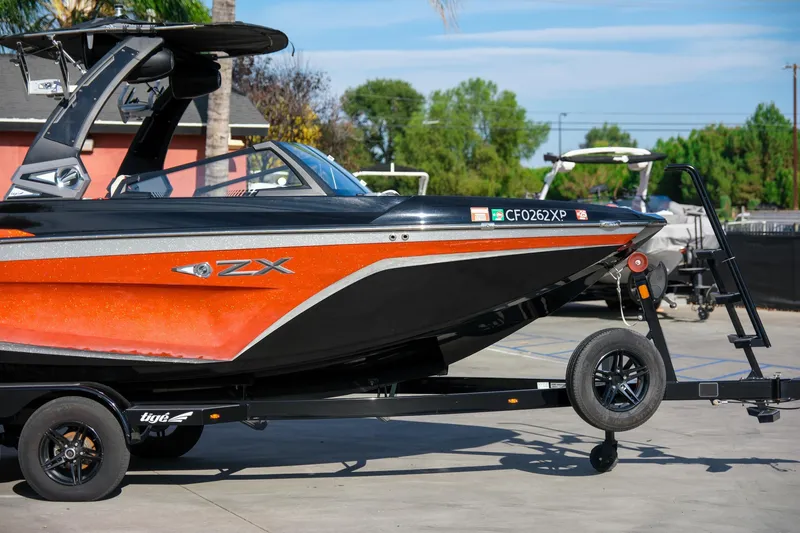 Slide: The Image of 2021 Tigé 21ZX boat on trailer, vibrant orange and black design, parked outdoors. - 7