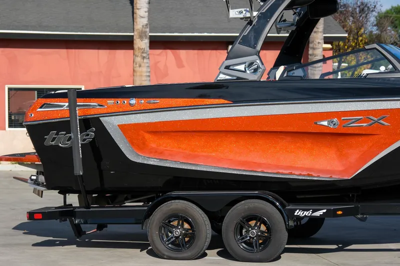 Slide: The Image of 2021 Tigé 21ZX boat with vibrant orange and black design on a trailer. - 8