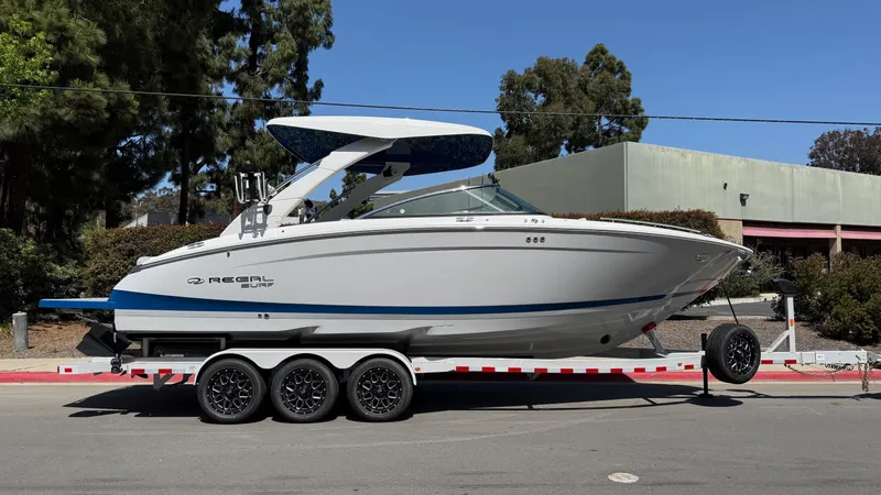 Slide: The Image of 2025 Regal LS9 Surf boat parked on a sunny street, rear view. - 10