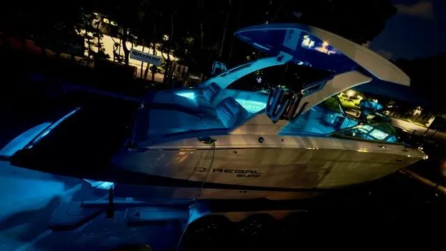 Slide: The Image of 2025 Regal LS9 Surf boat illuminated at night with blue LED lights. - 123