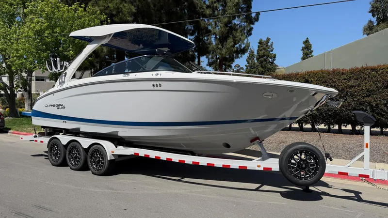 Slide: The Image of 2025 Regal LS9 Surf boat on a trailer, parked on a sunny street. - 13