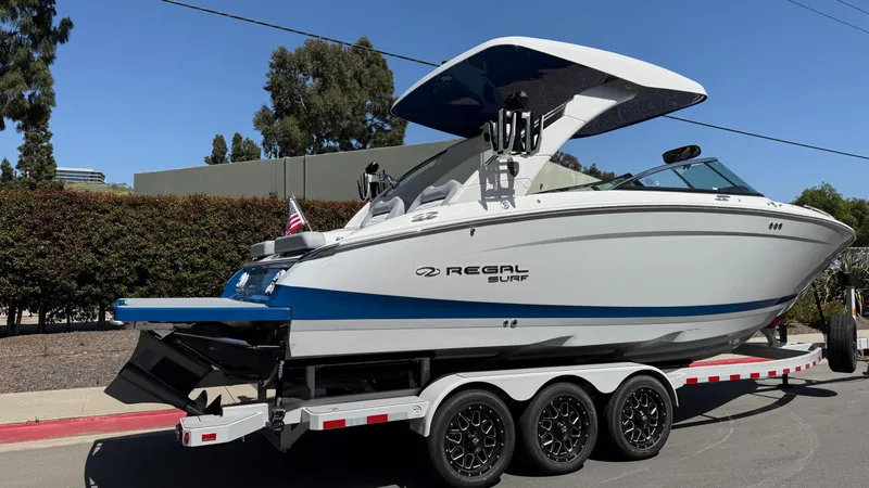 Slide: The Image of 2025 Regal LS9 Surf boat on a trailer, parked outdoors. - 17