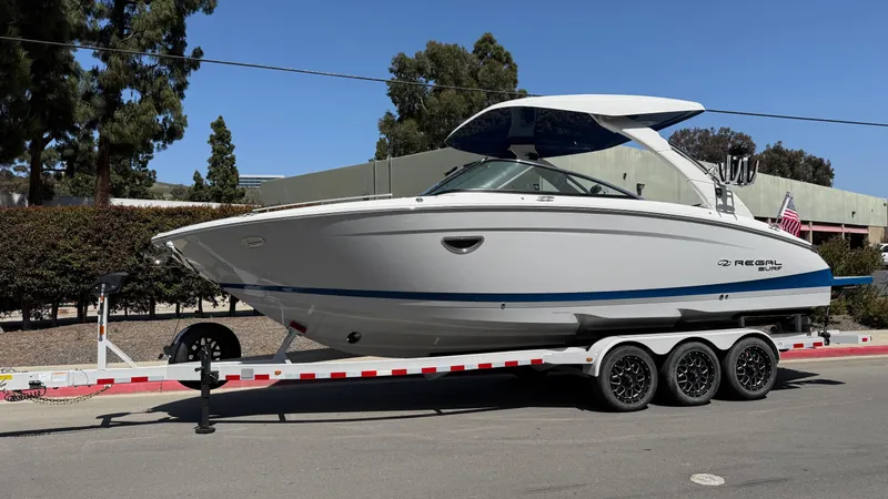 Slide: The Image of 2025 Regal LS9 Surf boat on a trailer, parked outdoors. - 2