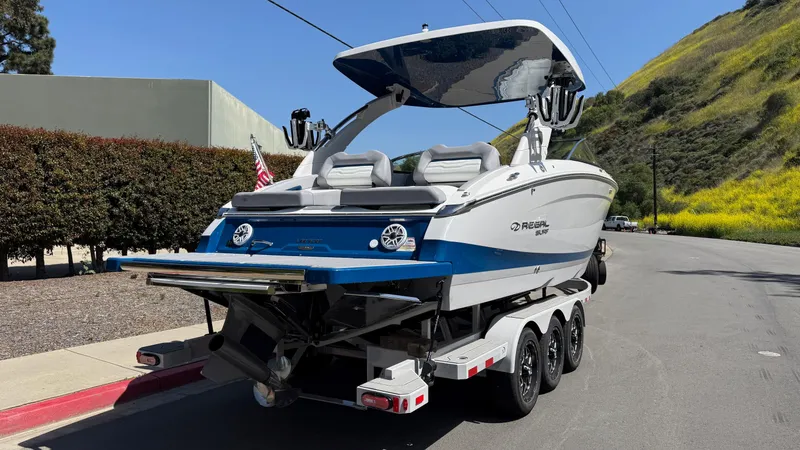 Slide: The Image of 2025 Regal LS9 Surf boat on trailer, parked on roadside with scenic background. - 20