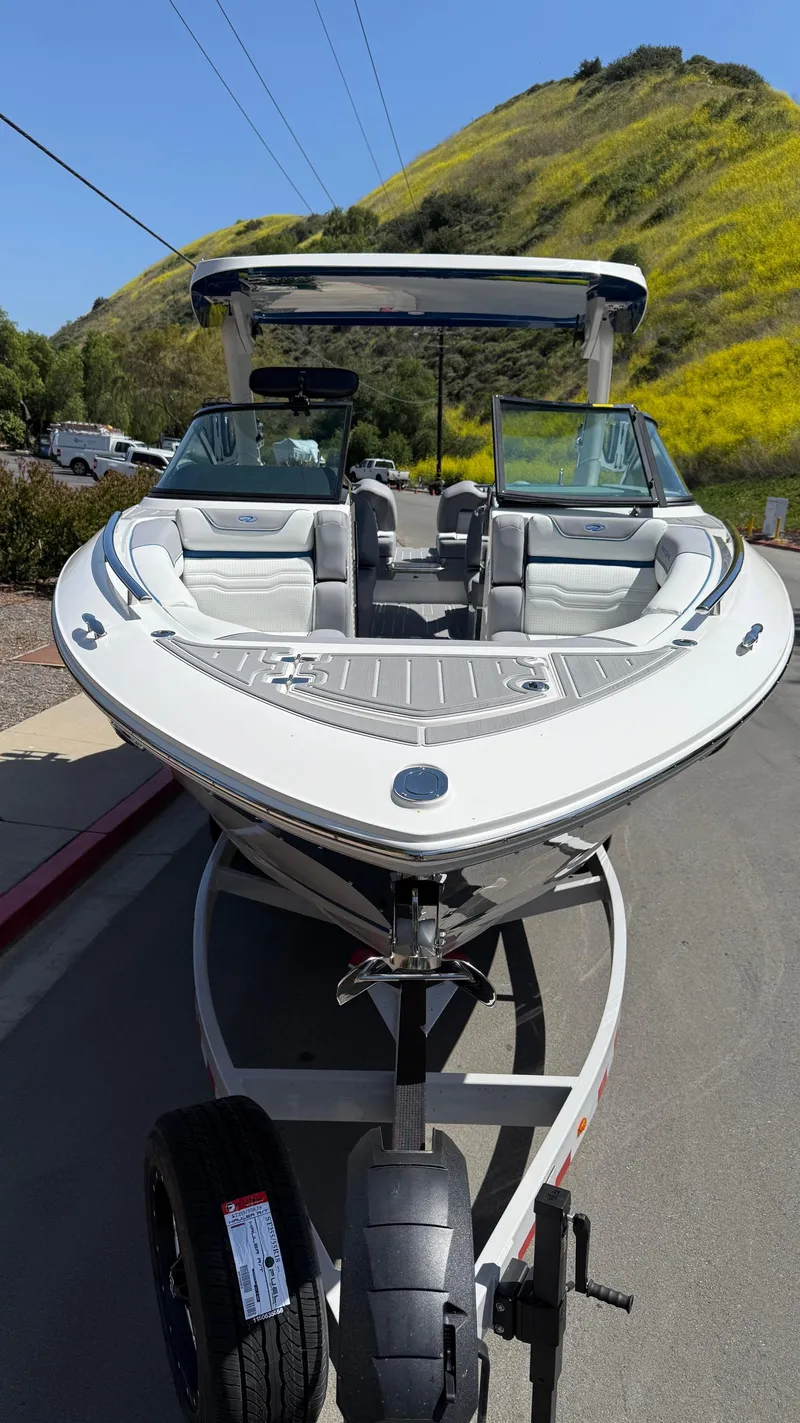 Slide: The Image of 2025 Regal LS9 Surf boat on trailer, parked on road with scenic hillside background. - 24