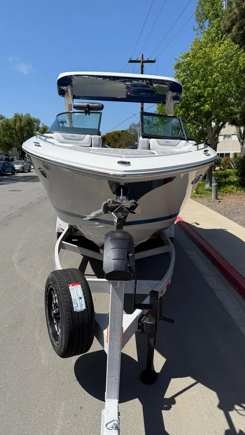 Slide: The Image of 2025 Regal LS9 Surf boat on trailer, parked on a sunny street. - 25