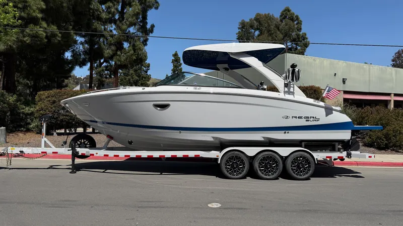 Slide: The Image of 2025 Regal LS9 Surf boat on a trailer, parked on a sunny street. - 3