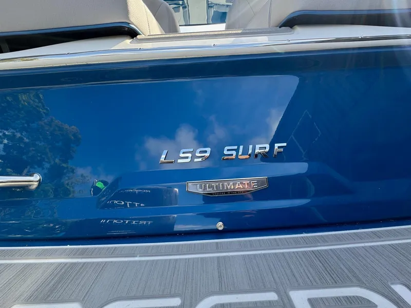Slide: The Image of 2025 Regal LS9 Surf boat, blue exterior with "Ultimate" badge, reflecting sky and trees. - 32