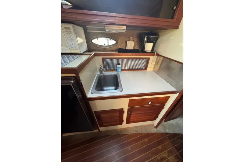 Slide: The Image of 1983 Tiara Yachts 3100 Open galley with sink, microwave, and wooden cabinetry. - 24