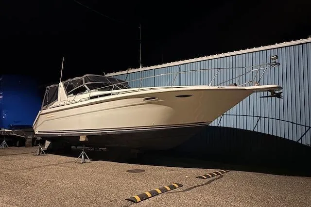 Slide: The Image of 1992 Sea Ray 370 Sundancer boat on stands, nighttime, near blue building. - 14