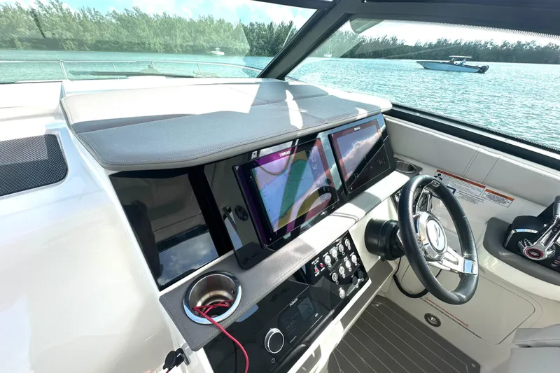 Slide: The Image of 2022 Sea Ray Sundancer 320 Outboard helm with dual displays and steering wheel, on calm water. - 33