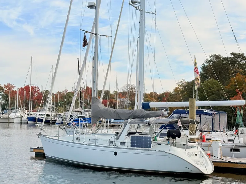 The Image of 1990 Beneteau 38 sailboat docked in a marina with autumn trees in the background. - 0