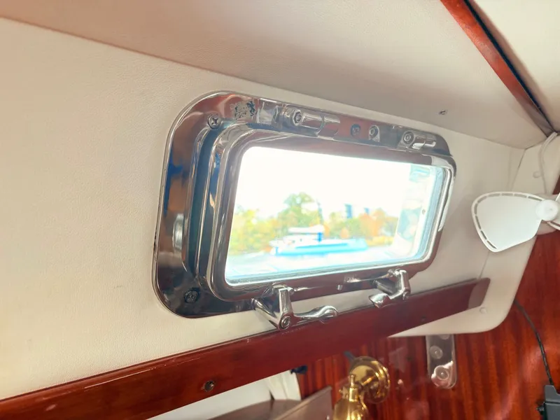 Slide: The Image of Portlight window inside a 1990 Beneteau 38 sailboat, featuring chrome handles and frame. - 50