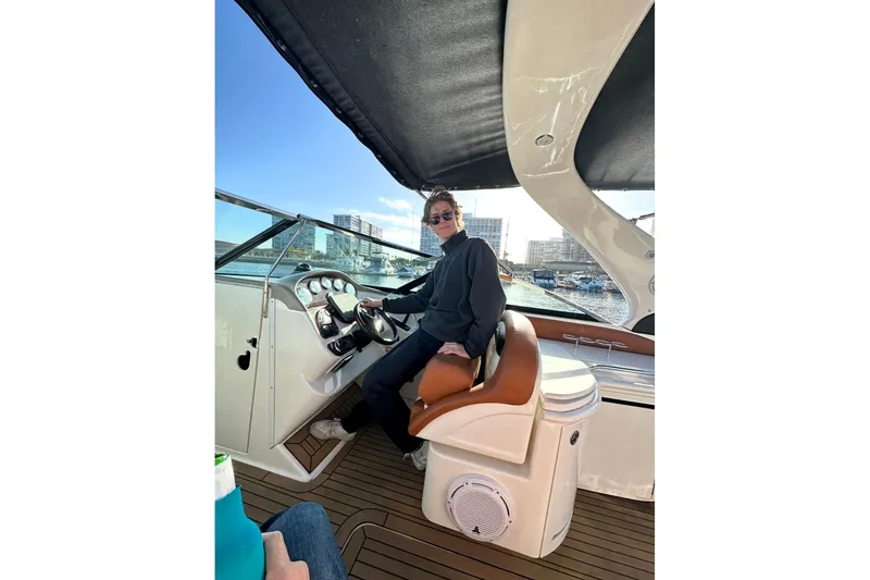 The Image of Person steering a 2008 Sea Ray 290 SLX boat, with cityscape in the background. - 1
