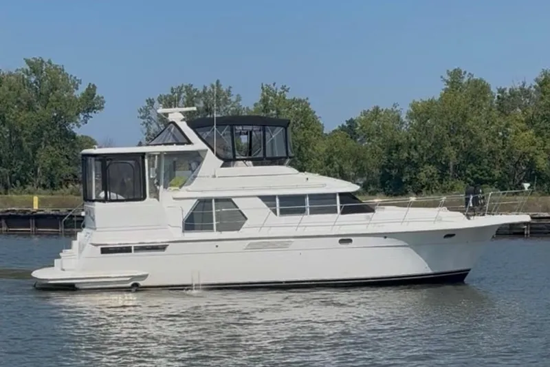 The Image of 1998 Carver 445 Aft Cabin Motor Yacht on calm water, surrounded by trees. - 0