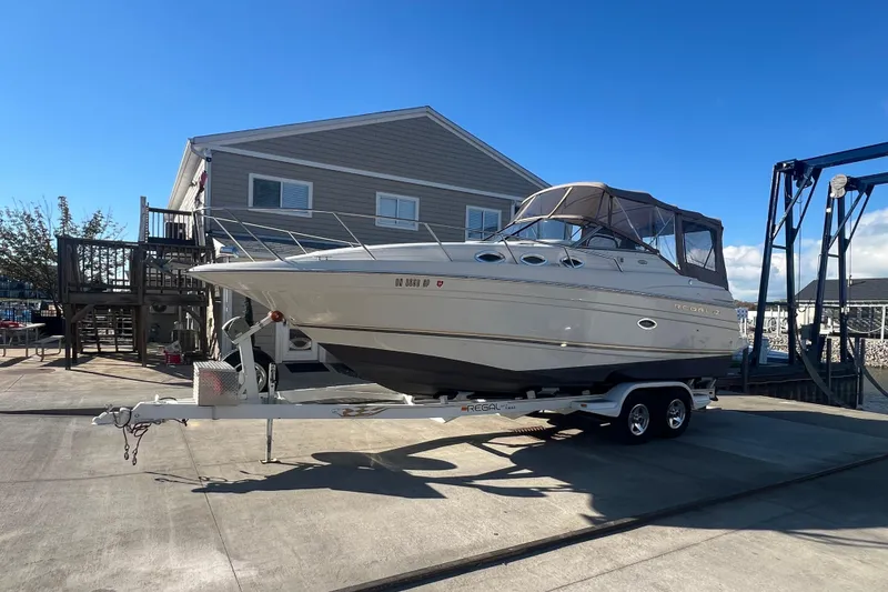 The Image of 2002 Regal Commodore 2765 boat on trailer, parked near a building under clear blue sky. - 0