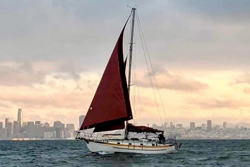 Slide: The Image of 1978 Tayana 37 sailboat with red sails on a city skyline backdrop. - 1