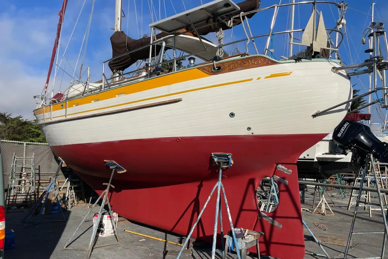Slide: The Image of 1978 Tayana 37 sailboat on dry dock, featuring a red hull and white upper deck. - 37