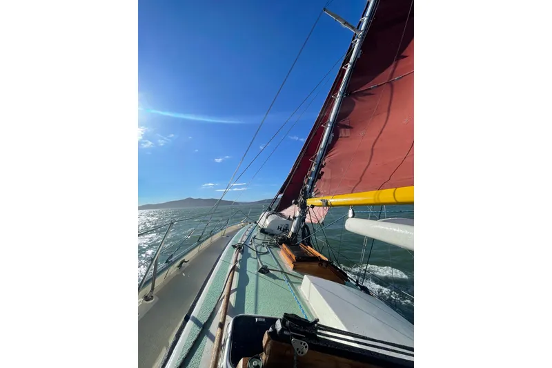 Slide: The Image of 1978 Tayana 37 sailboat with red sails on open water under clear blue sky. - 5