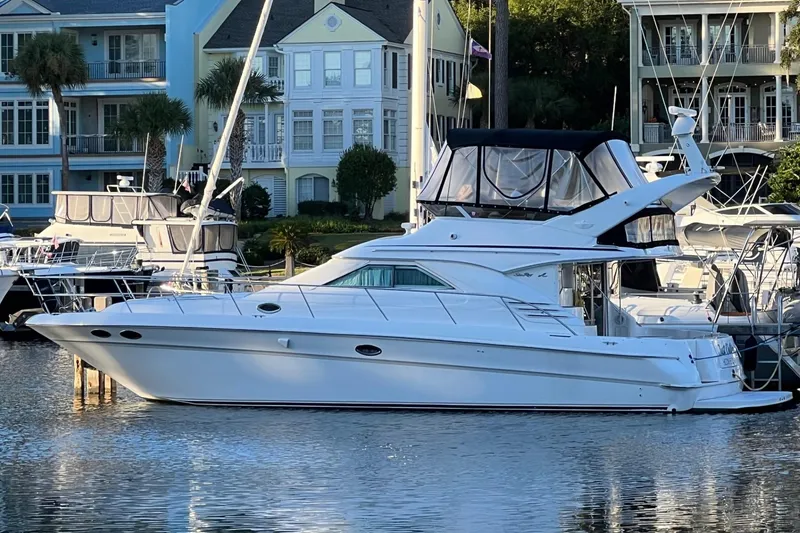 The Image of 2000 Sea Ray 400 Sedan Bridge yacht docked in a marina, surrounded by waterfront homes. - 0