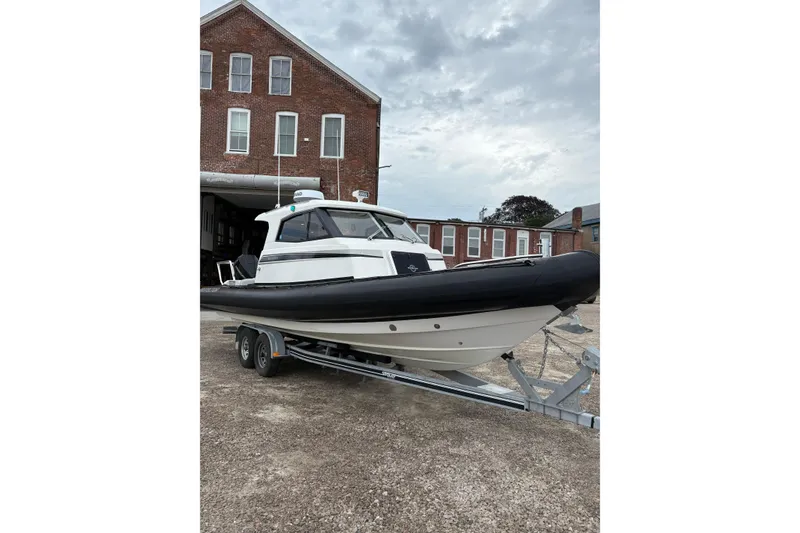 Slide: The Image of 2020 Protector 310 Targa boat on trailer, parked near brick building under cloudy sky. - 4