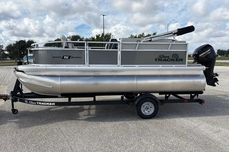 The Image of 2026 Sun Tracker Bass Buggy 16 XL Select pontoon boat on trailer, parked outdoors. - 0