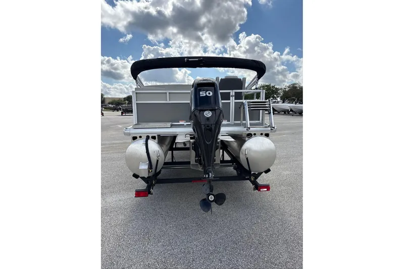 Slide: The Image of 2026 Sun Tracker Bass Buggy 16 XL Select pontoon boat, rear view with motor, under cloudy sky. - 2