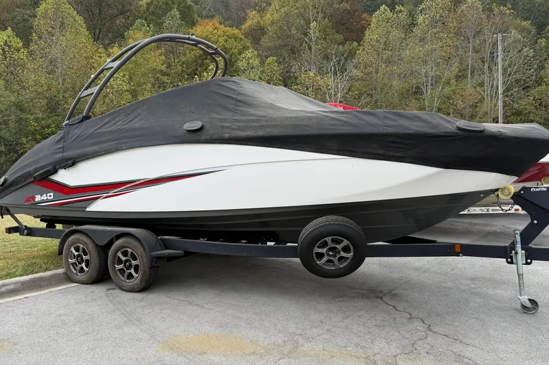 Slide: The Image of 2019 Yamaha Boats AR240 covered on trailer, parked outdoors with forest background. - 14