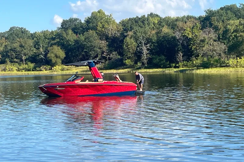 The Image of 2021 Nautique Super Air Nautique G23 Paragon on a serene lake with lush forest backdrop. - 0