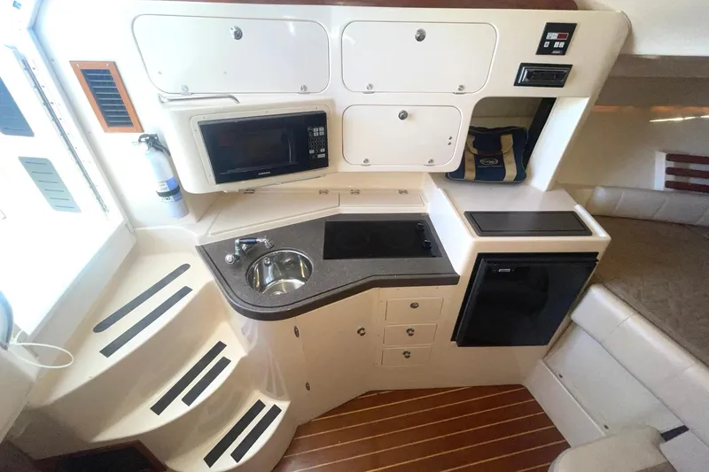 Slide: The Image of 2003 Grady-White Express 330 cabin with kitchenette, featuring sink, microwave, and compact fridge. - 24