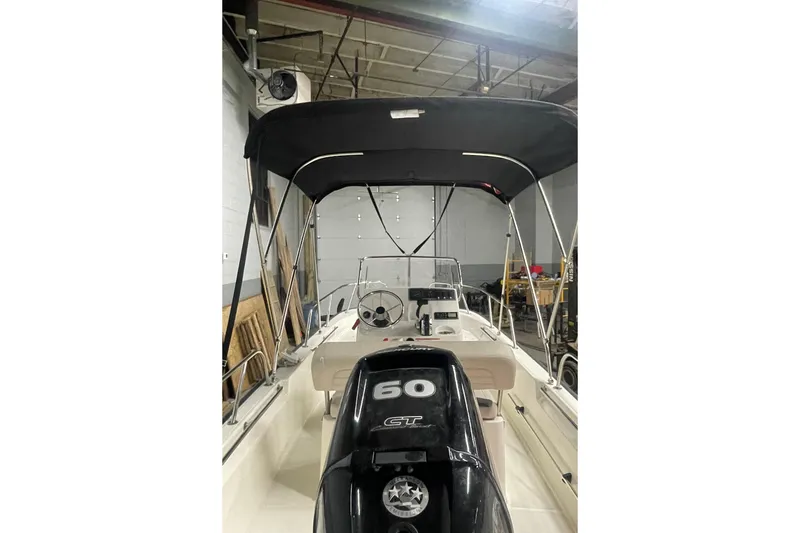 Slide: The Image of 2021 Boston Whaler 150 Montauk boat with canopy and outboard motor in a garage. - 14