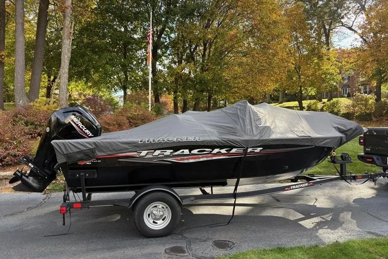 The Image of 2023 Tracker Pro Guide V-16 SC boat covered, parked on trailer in scenic autumn setting. - 1