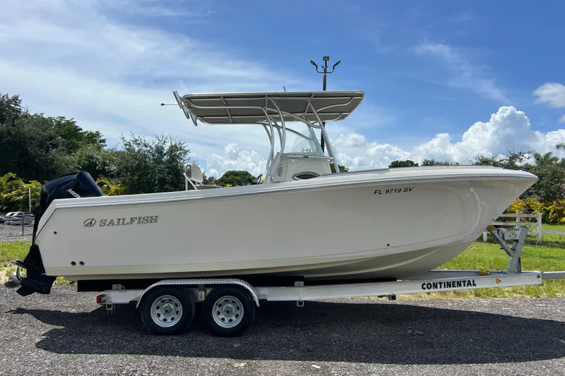 Slide: The Image of 2021 Sailfish 242 CC boat on trailer, parked outdoors under a clear blue sky. - 0