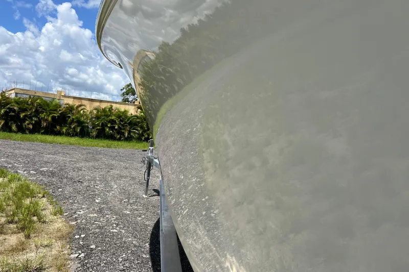 Slide: The Image of 2021 Sailfish 242 CC boat reflecting greenery and sky, parked on gravel. - 7