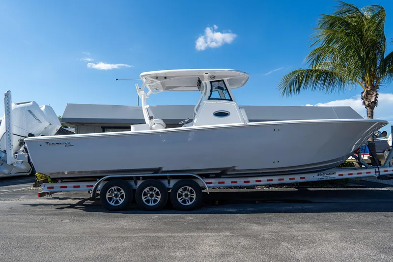 Slide: The Image of 2026 Tidewater 3100 Carolina Bay boat on trailer, parked near palm tree under clear sky. - 0