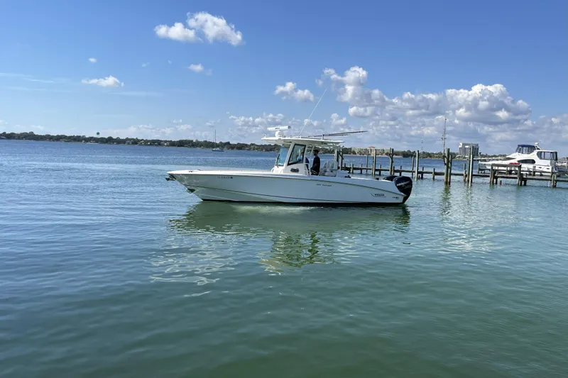 Slide: The Image of 2012 Boston Whaler 320 Outrage boat on calm water near a dock under a clear sky. - 2