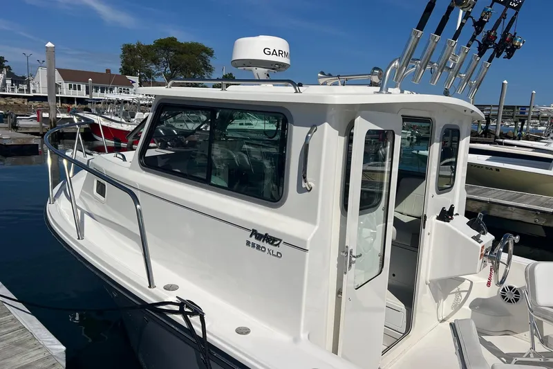 Slide: The Image of 2023 Parker 2520 XLD Sport Cabin boat docked at marina with fishing rods. - 2