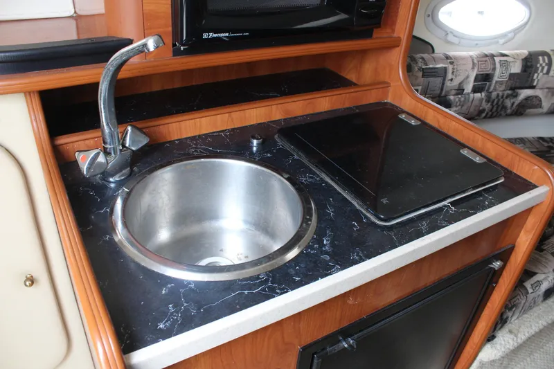 Slide: The Image of 2002 Rinker Fiesta Vee 250 boat kitchenette with sink, stove, and wood finish. - 26