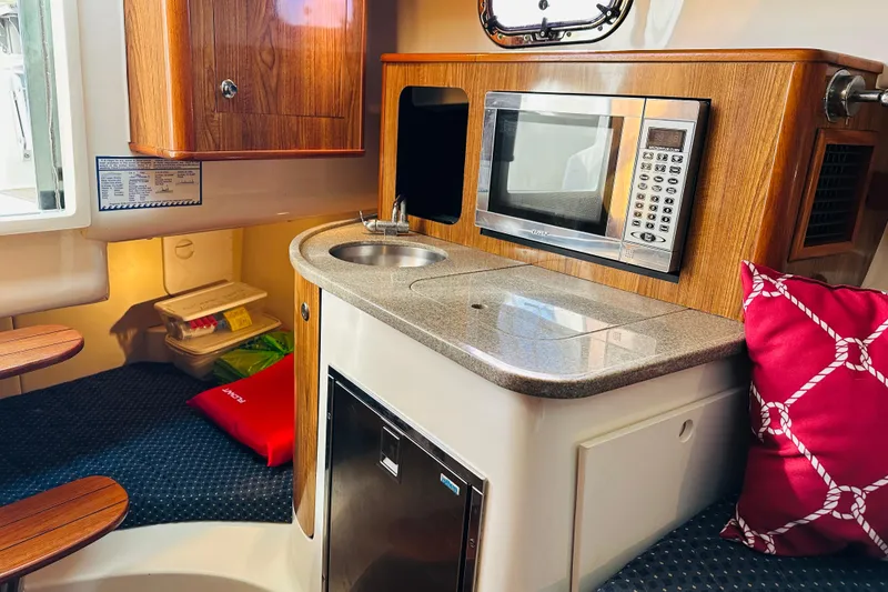 Slide: The Image of 2007 Pursuit OS 285 Offshore cabin with kitchenette, microwave, sink, and red cushion. - 31